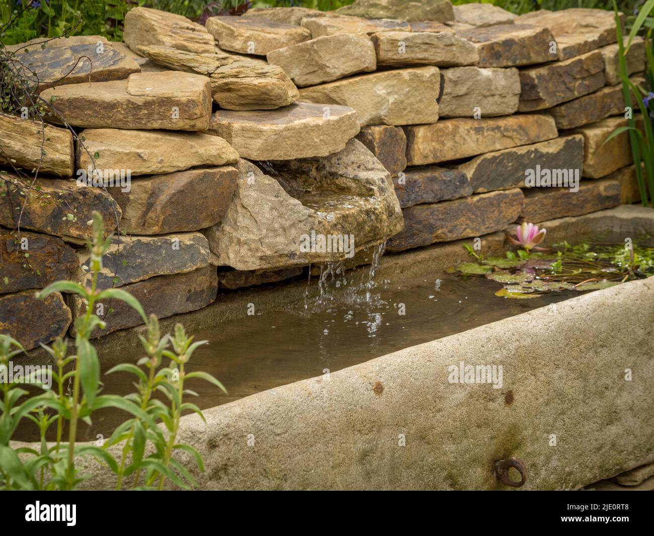 Élément d'eau dans un mur sec s'écoulant dans une vieille cuvette d'eau dans un jardin britannique. Banque D'Images