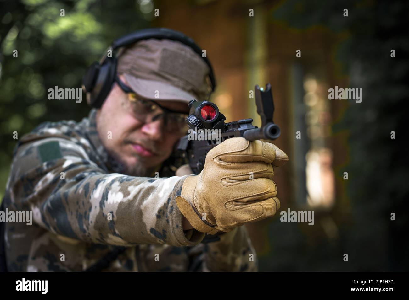 Tireur avec un fusil dans un casque de protection auditive tactique uniforme militaire. Formation de la police dans la galerie de tir avec arme. Homme de police civile en formation tactique. Mise au point sélective à portée de main. Banque D'Images