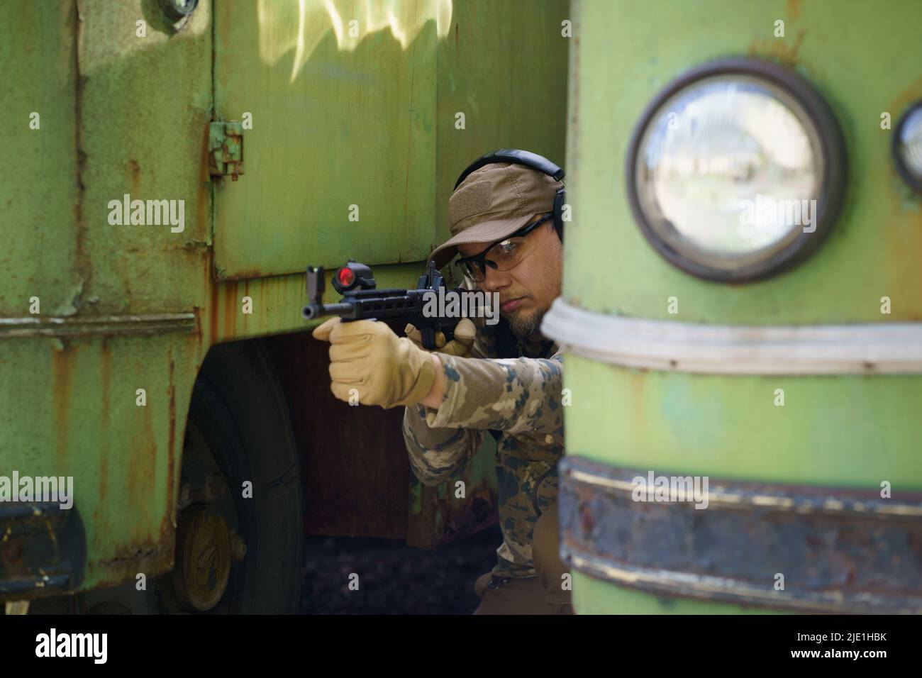 Entraînement aux troubles civils, l'homme en cours d'entraînement tactique se cache derrière les vieux véhicules rouillés. Formation de policiers à l'usine de tir avec arme. Cours d'entraînement tactique de l'homme de trooper commandé. Banque D'Images