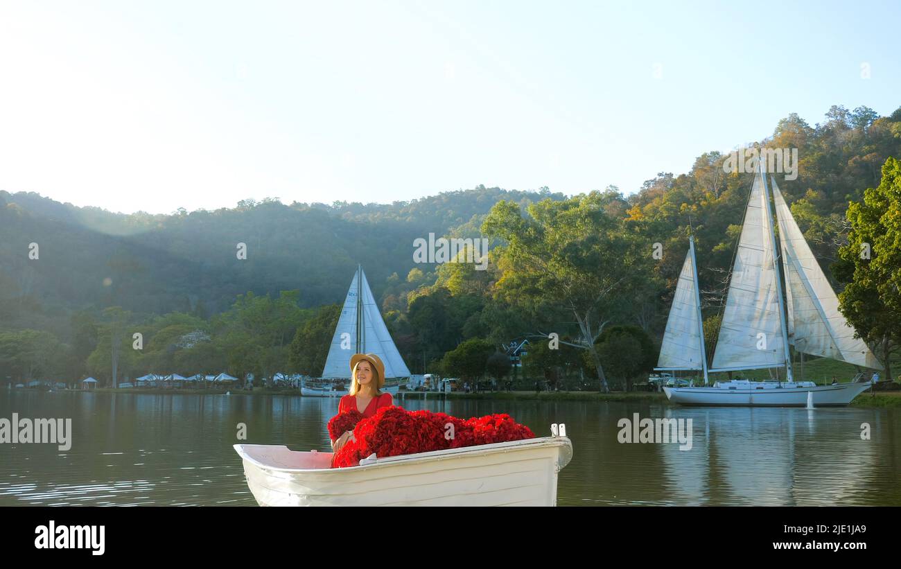 Vacances romantiques. Femme élégante en robe rouge le jour, assise dans le bateau Banque D'Images
