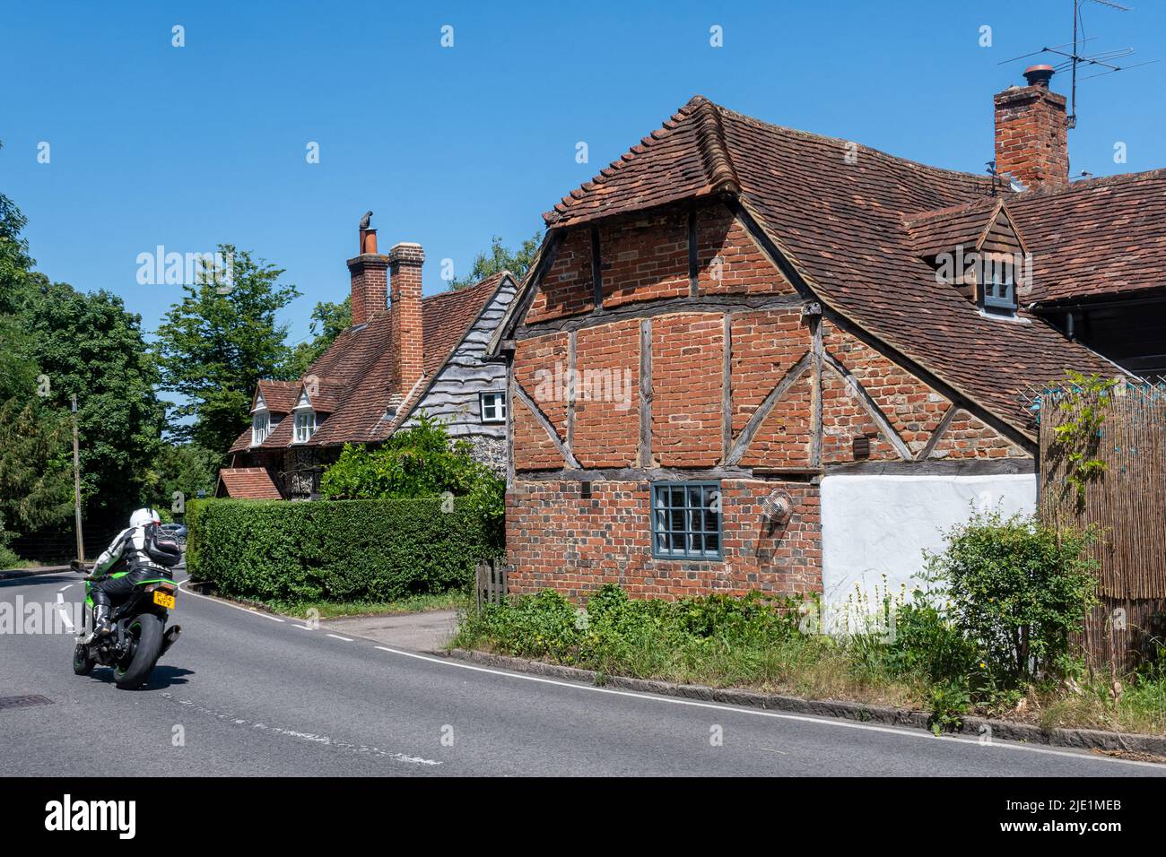 West Clandon village, Surrey, Angleterre, Royaume-Uni, avec un motocycliste passant devant des bâtiments ou des maisons historiques Banque D'Images