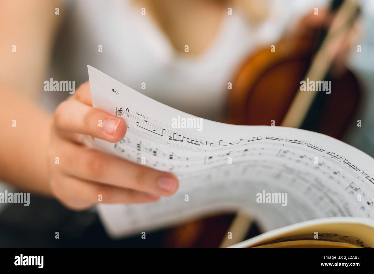 Gros plan main de femme caucasienne tournant la page de partitions de musique sur le stand de musique, femme violoniste floue en arrière-plan, avec espace de copie. Banque D'Images