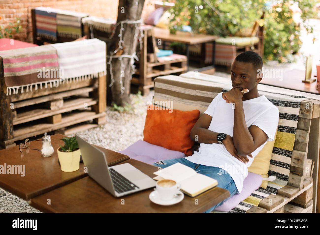 Un homme d'affaires multiracial concentré et déroutant s'assoit sur le banc avec un ordinateur portable dans un café de rue, lisant des données sans oublier Banque D'Images