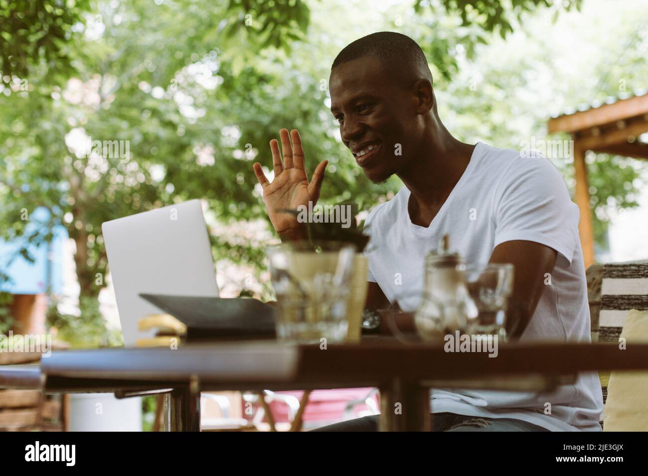 Souriant et heureux homme multiracial avec ordinateur portable, levant le bras, saluer quelqu'un, regardant le moniteur. Séminaire en ligne sur l'apprentissage en ligne Banque D'Images