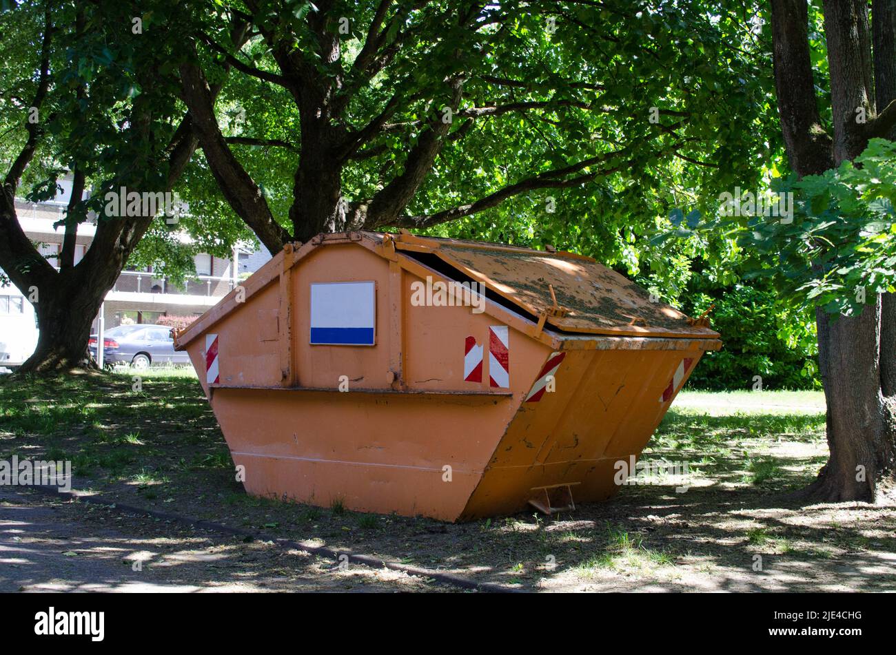 contenant orange pour les déchets volumineux ou les décombres de bâtiment avec un panneau blanc vide avec espace de texte entre les arbres lors d'une journée ensoleillée en été Banque D'Images