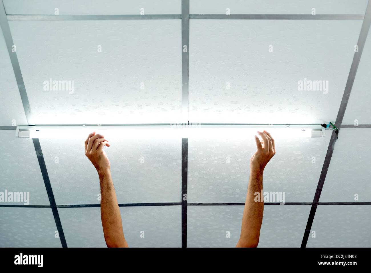 Gros plan de la main d'un homme qui installe une longue ampoule LED au plafond. Banque D'Images Gros plan de la main d'un homme qui installe une longue ampoule LED au plafond. Banque D'Images