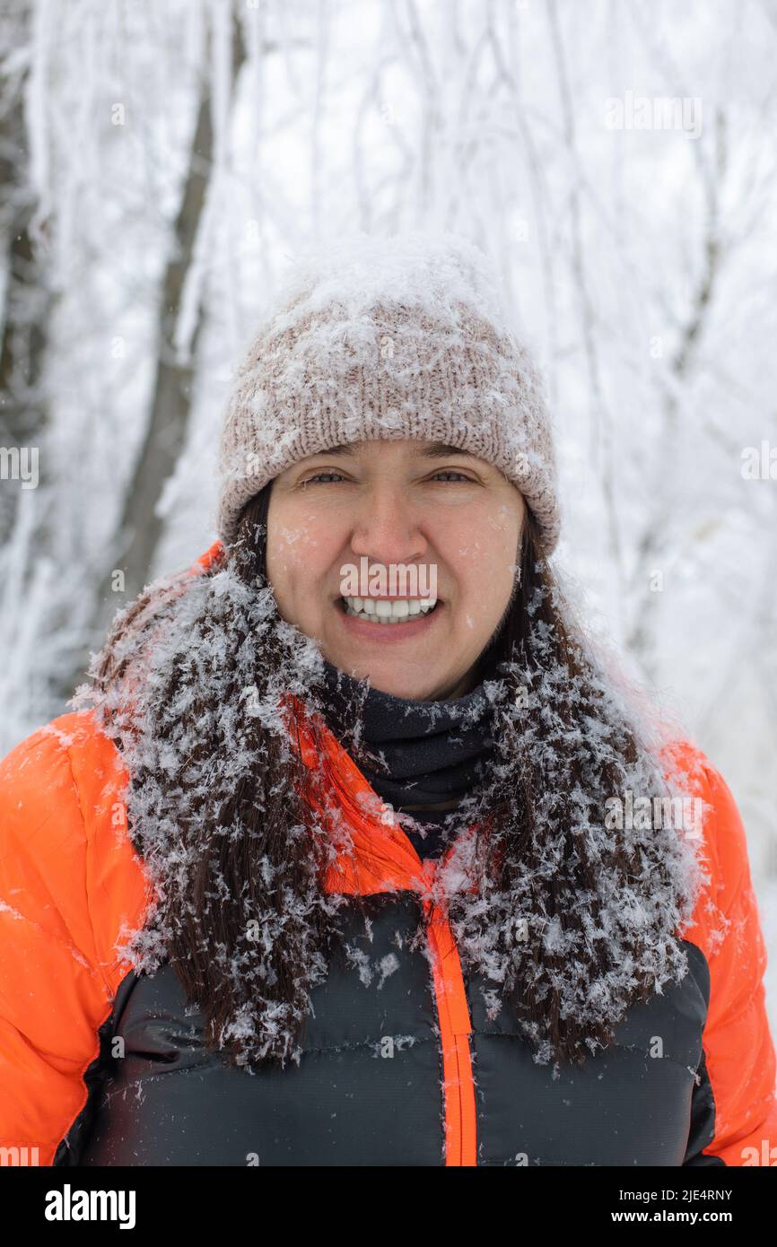 Portrait d'une femme gelée souriant regardant l'appareil photo souriant vêtu de vêtements chauds d'hiver avec des cheveux et un chapeau recouvert de neige. Plein de vacances d'hiver Banque D'Images