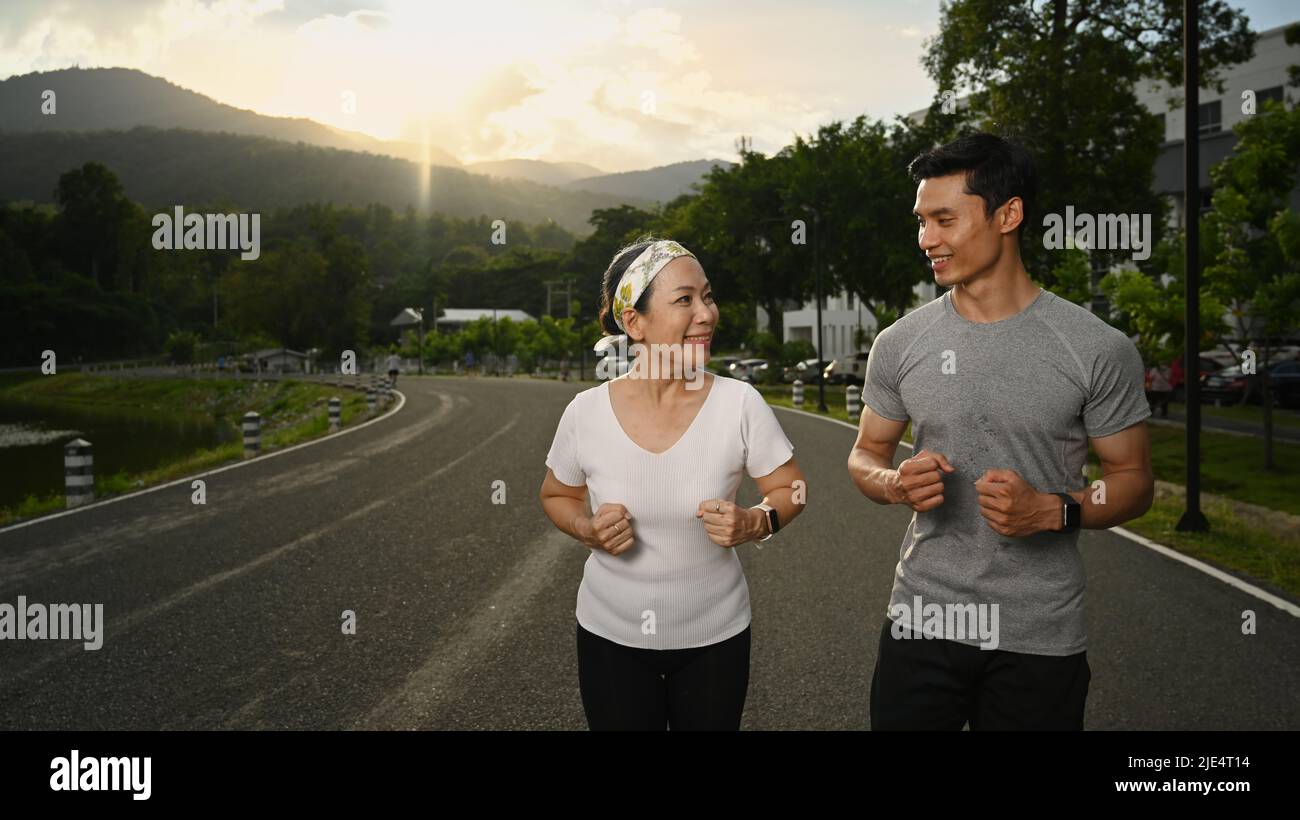Une femme énergique et mature, et son entraîneur personnel, qui fait du jogging dans le parc de la ville le soir. Mode de vie sain et concept de forme physique Banque D'Images