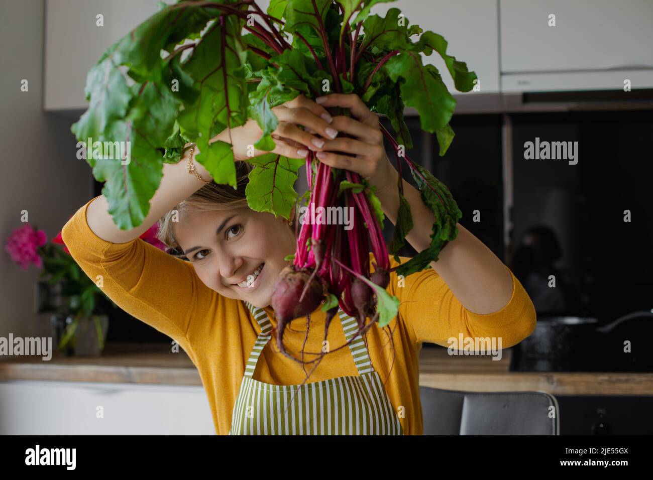 Femme blonde souriante tenant un bouquet de betteraves, cuisant de la salade saine biologique fraîche dans la cuisine en été. Nourriture écologique Banque D'Images