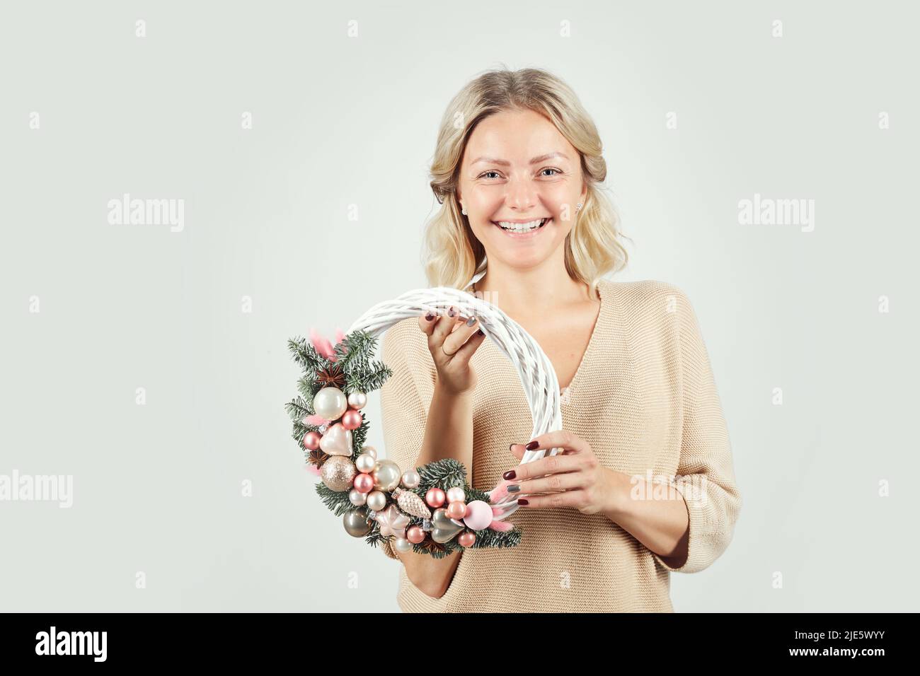 Portrait de gaie excitée belle jeune femme avec des cheveux blonds debout sur un fond isolé et tenant une couronne de Noël artificielle Banque D'Images