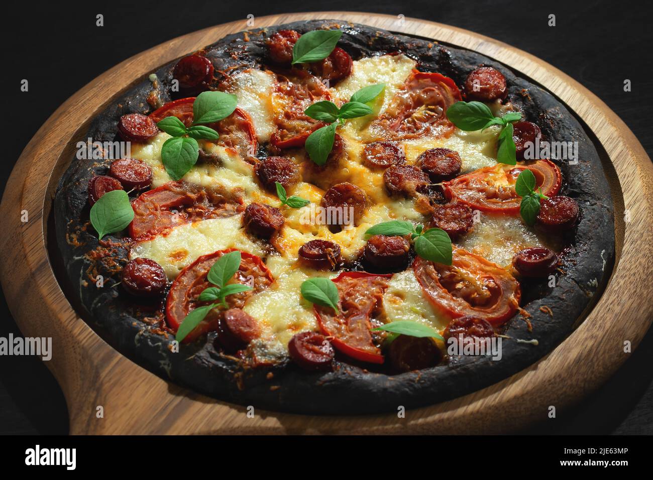 Pizza noire avec tomates, saucisses, mozzarella et basilic.Pâte à base de poudre de charbon de bambou saine. Banque D'Images