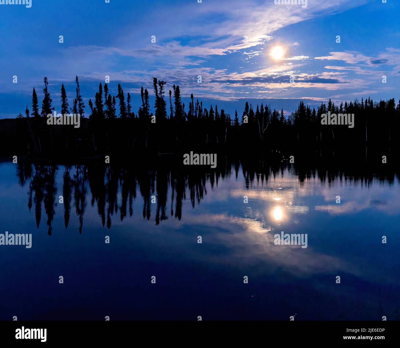 Une pleine lune du nord de la Saskatchewan se reflète dans les eaux d'un lac. Banque D'Images