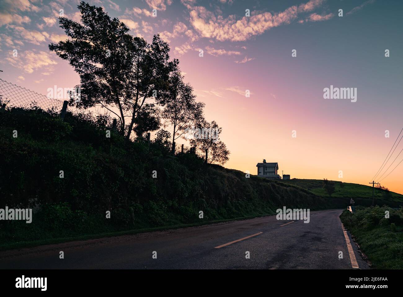 Une vue colorée du ciel de lever du soleil avec ciel rose et bleu avec arbre et maison comme silhouette Banque D'Images