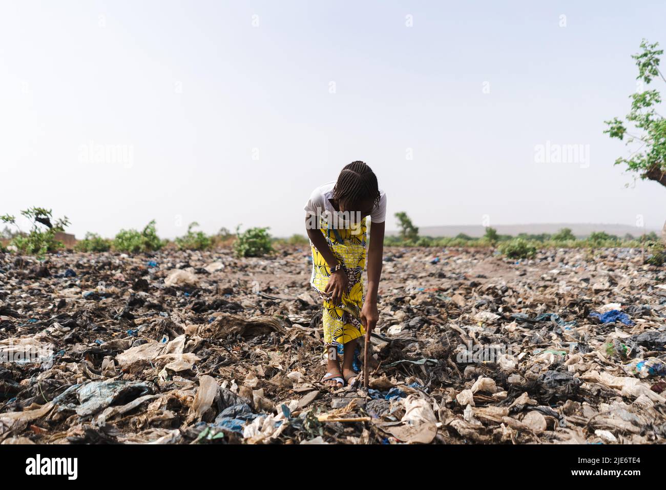 Une jeune fille africaine creuse dans un dépotoir à la recherche de matériaux réutilisables ; recyclage informel des déchets Banque D'Images