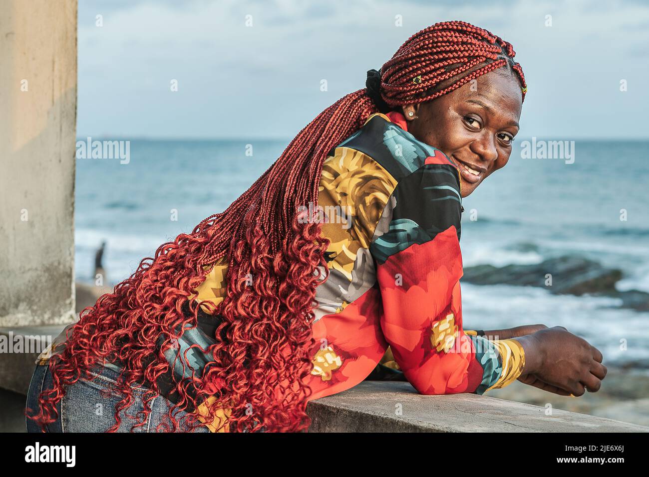 Femme africaine avec de beaux cheveux rasta rouges surplombant la mer depuis un balcon à Accra Ghana Afrique de l'Ouest Banque D'Images