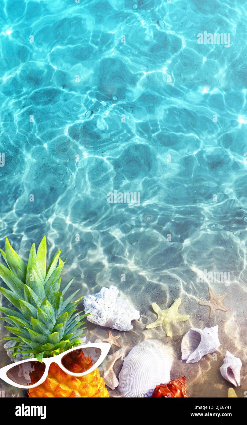 Ananas mûr dans des lunettes de soleil élégantes et coquillages dans la mer bleue, détente. Concept de vacances tropicales d'été. Banque D'Images