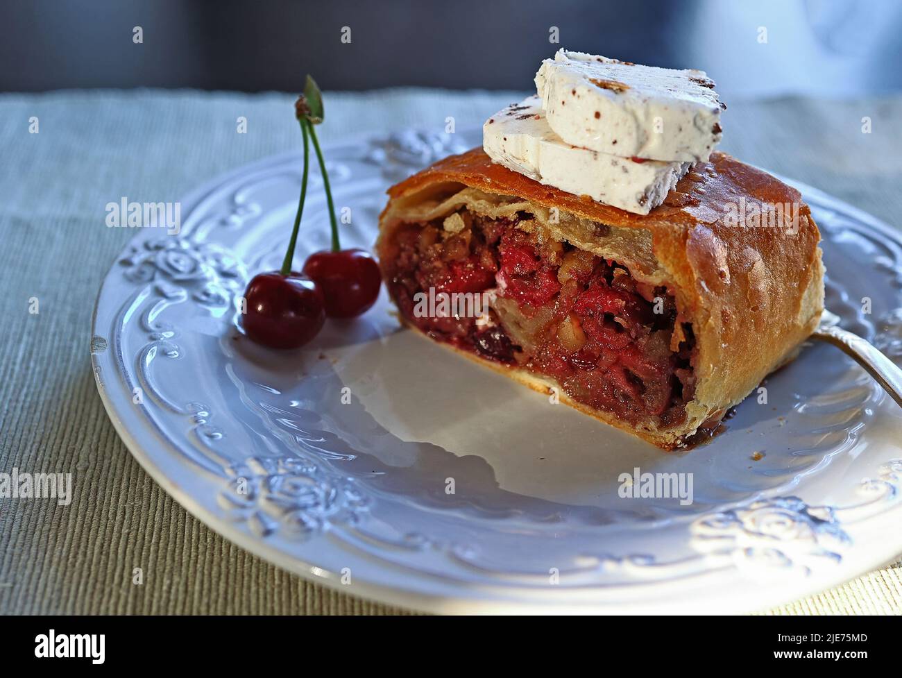 Tranché de strudel maison avec des cerises et une tranche de crème glacée, gros plan sur une assiette blanche. Tranche de strudel maison fraîchement cuit avec des cerises et W Banque D'Images