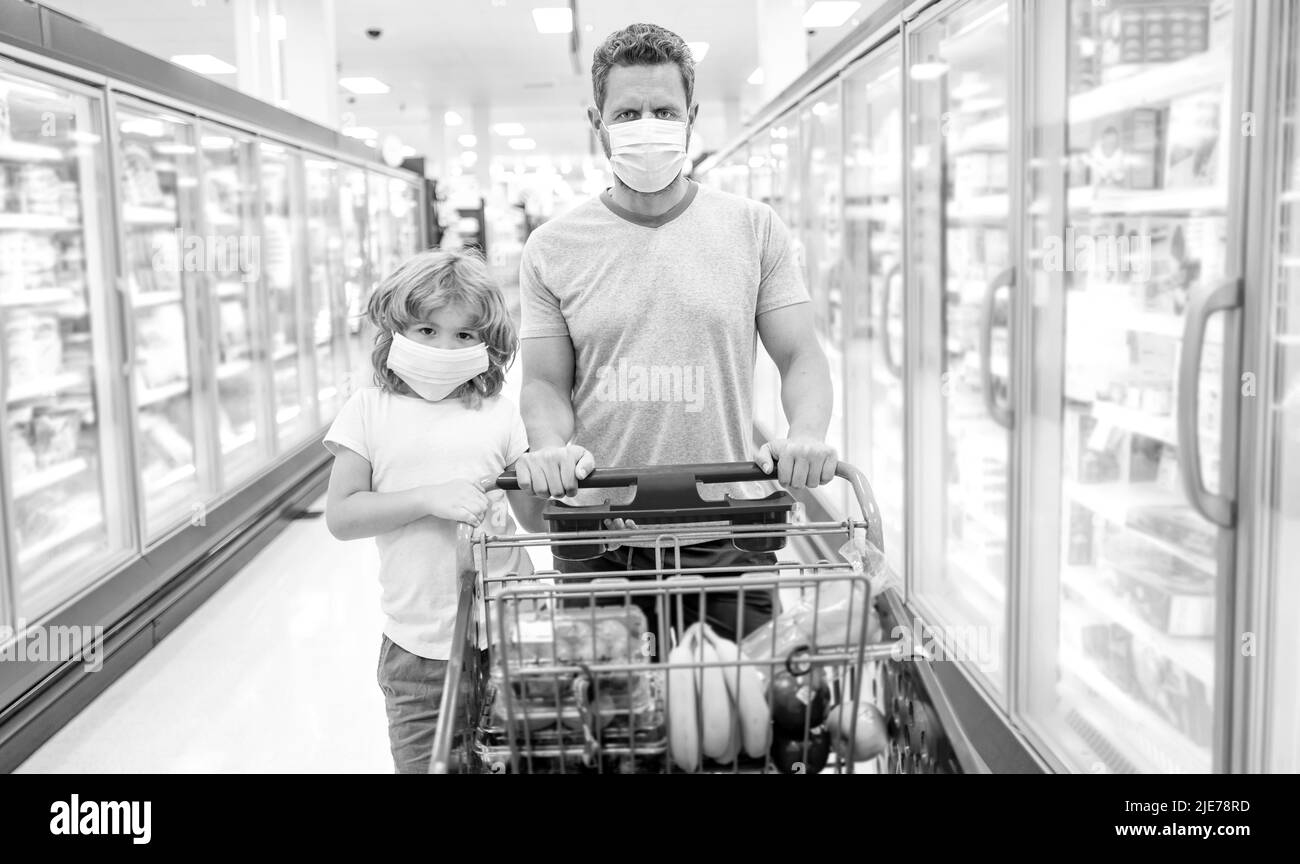 famille heureuse de père et de fils dans le masque de protection avec panier d'achat de nourriture, consumérisme Banque D'Images