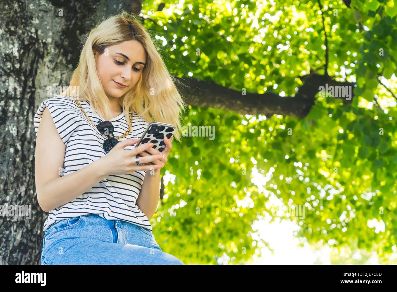 Caucasienne fille assise sous l'arbre et en utilisant son téléphone mobile. Cowboy tourné concept de technologie extérieure. Photo de haute qualité Banque D'Images