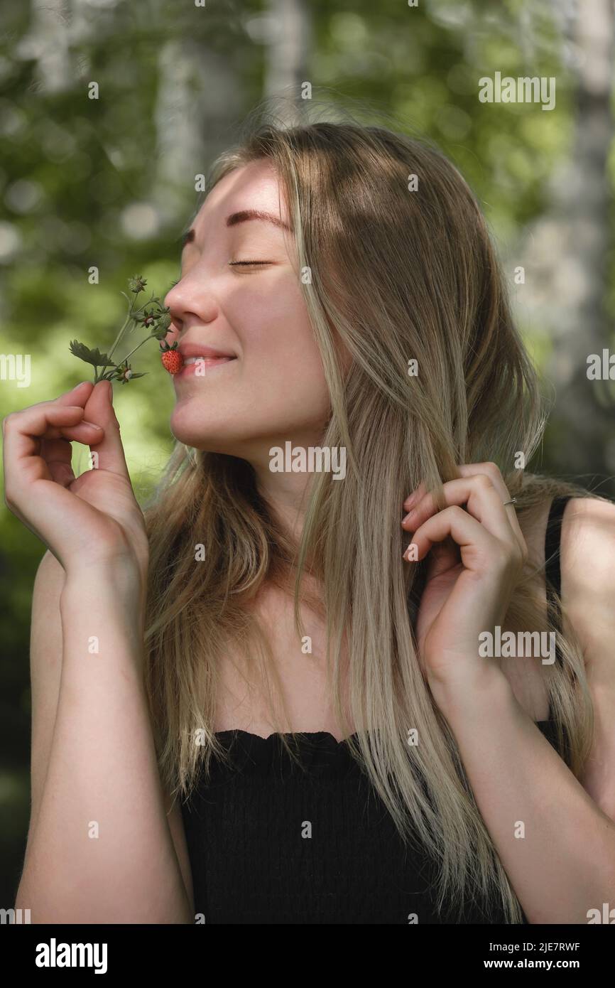 Femme sentant des fraises sauvages dans la forêt. Baies rouges mûres dans la nature pleine de vitamines. Activités d'été de loisirs pour les personnes en plein air. Gros plan Banque D'Images