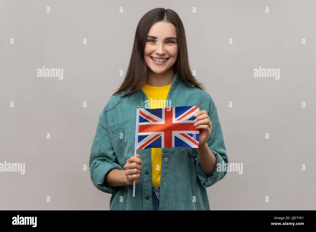 Portrait d'une femme ravie tenant le drapeau britannique, regardant l'appareil photo avec un sourire crasseux, patriote, portant une veste de style décontracté. Prise de vue en studio isolée sur fond gris. Banque D'Images