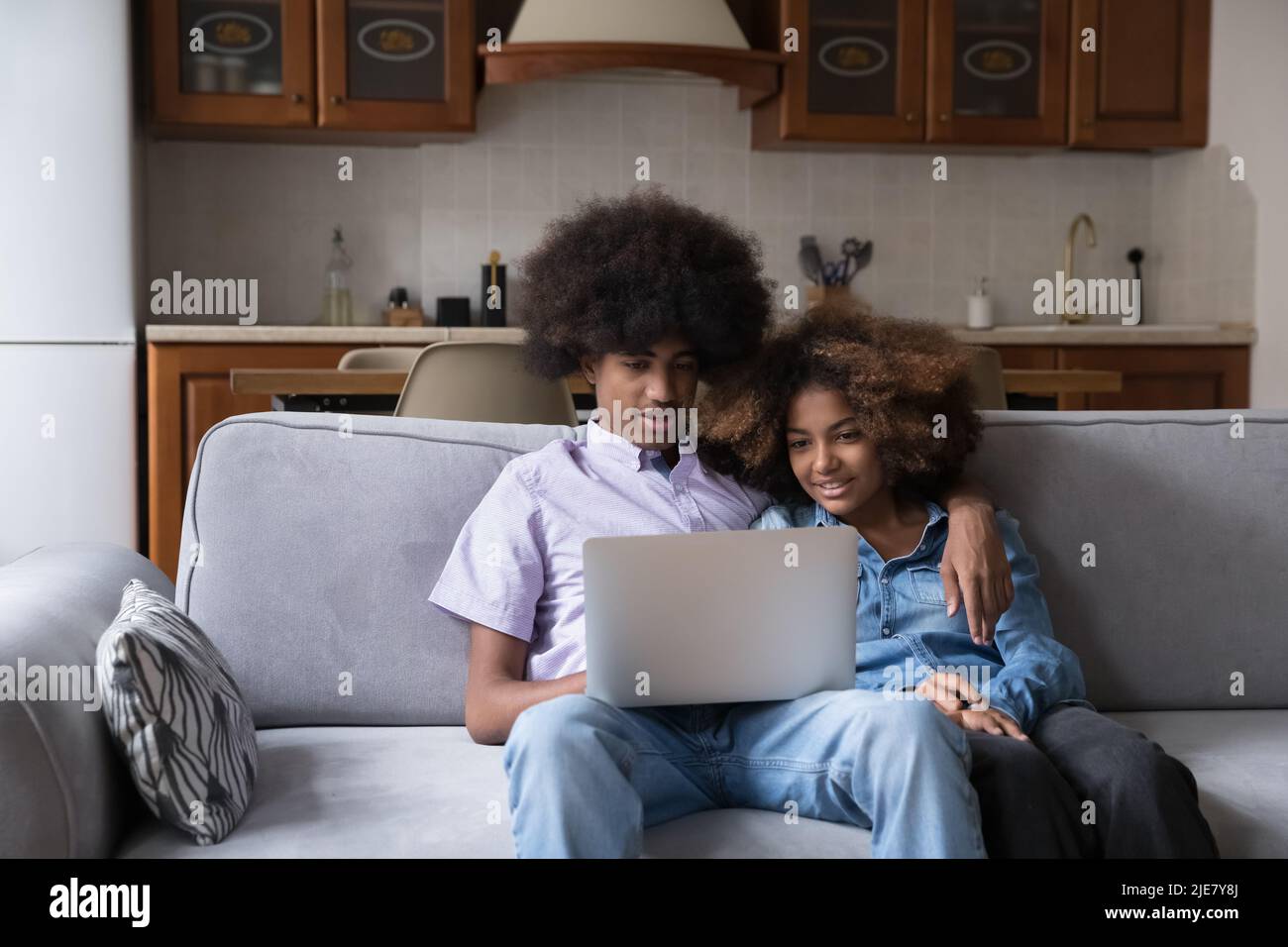 Un beau couple africain adolescent s'assoit sur un canapé avec un ordinateur portable Banque D'Images