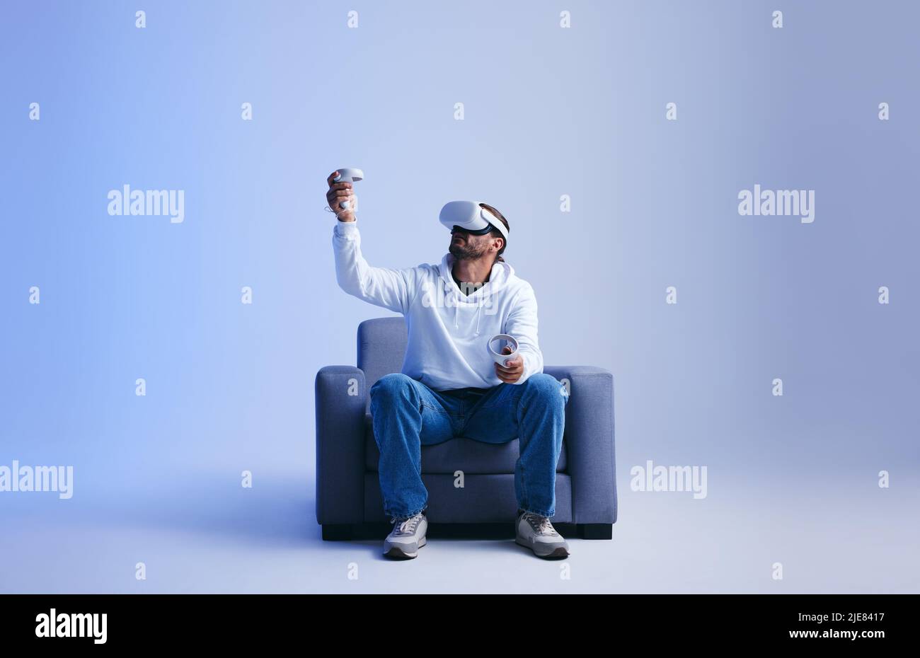 Jeune homme jouant un jeu de réalité virtuelle immersif sur un canapé. Homme jouant avec des lunettes de réalité virtuelle et des contrôleurs. Jeune homme qui vit un 3D s. Banque D'Images