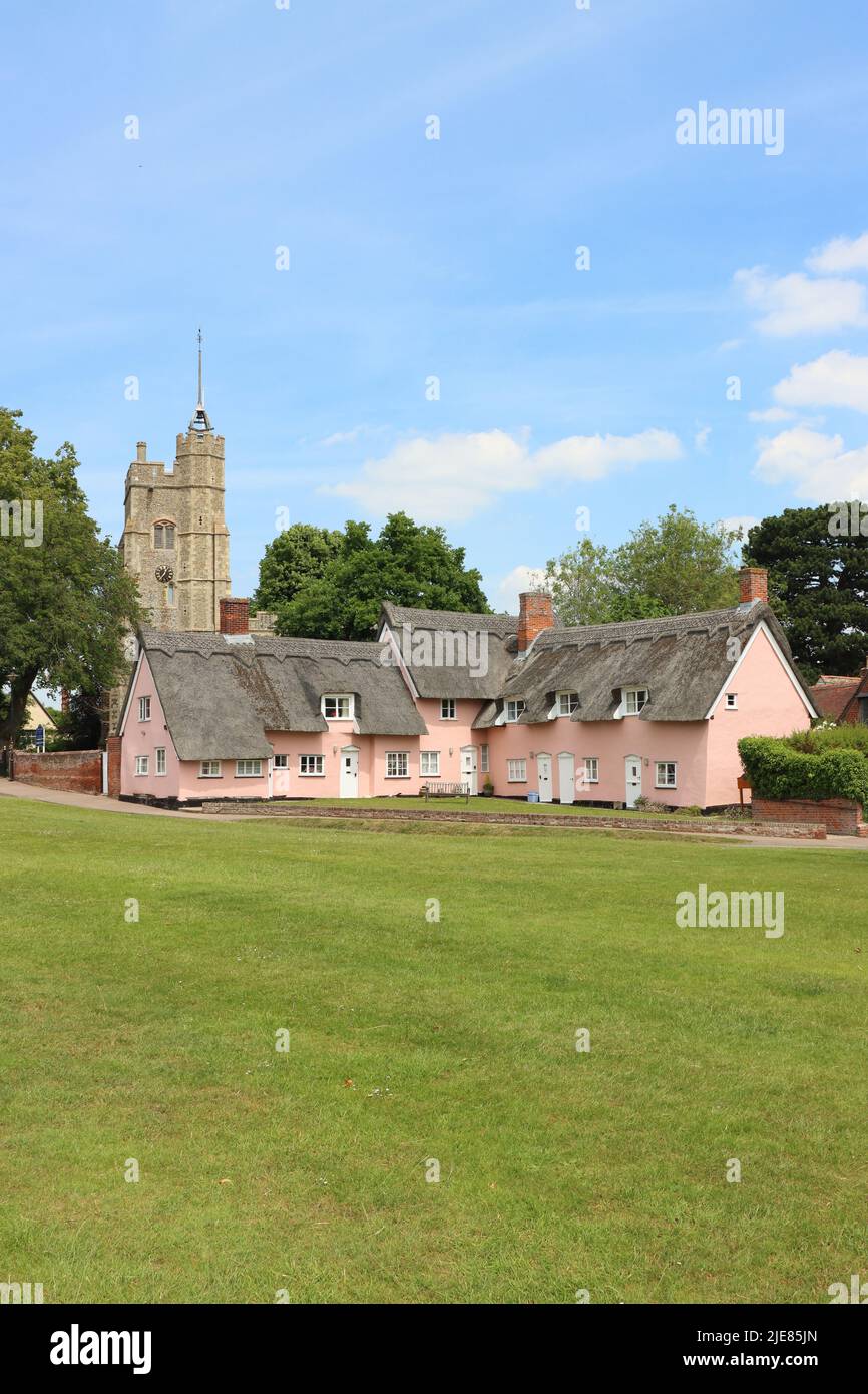 Chalets de chaume peints en rose avec l'église Sainte-Marie-la-Vierge sur le vert du village. Cavendish, Suffolk, East Anglia, Royaume-Uni Banque D'Images