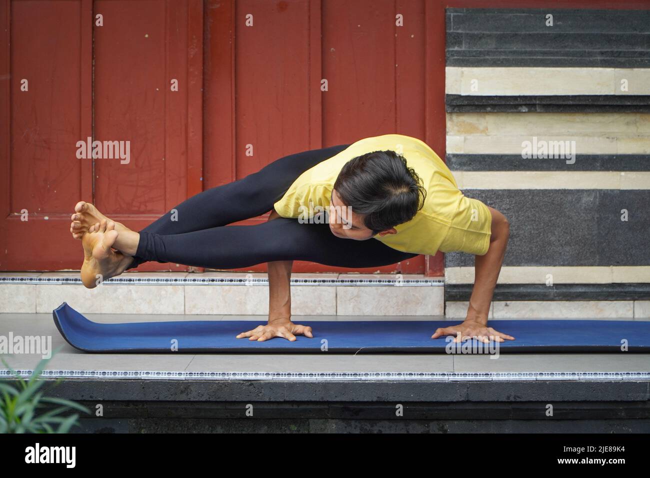 Sur sa terrasse, une jeune fille asiatique d'apparence étonnante pratique le yoga tout en portant une coupe courte, une chemise jaune et des leggings noirs. S Banque D'Images