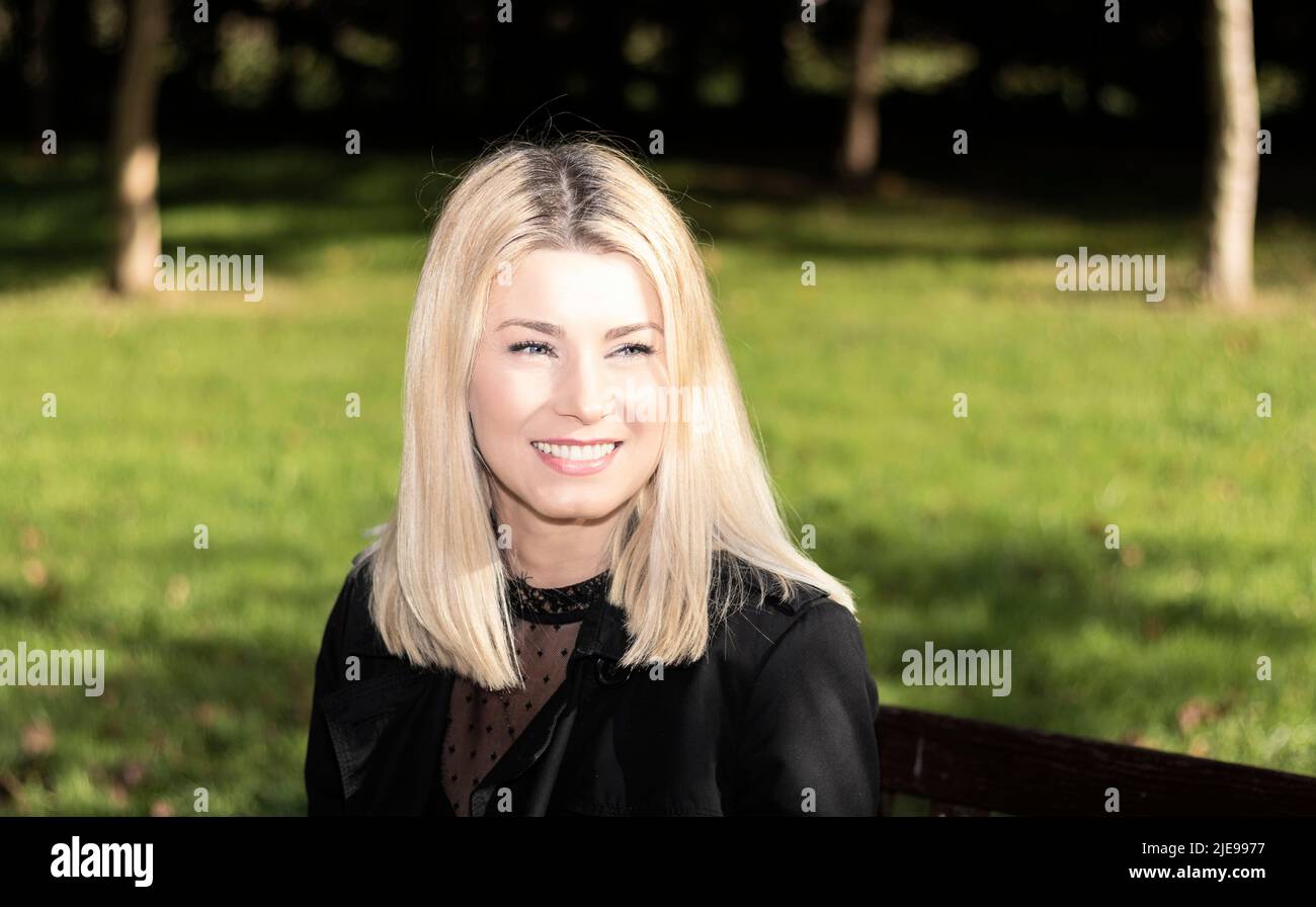 belle femme blonde assise sur un banc souriante vêtue de noir Banque D'Images