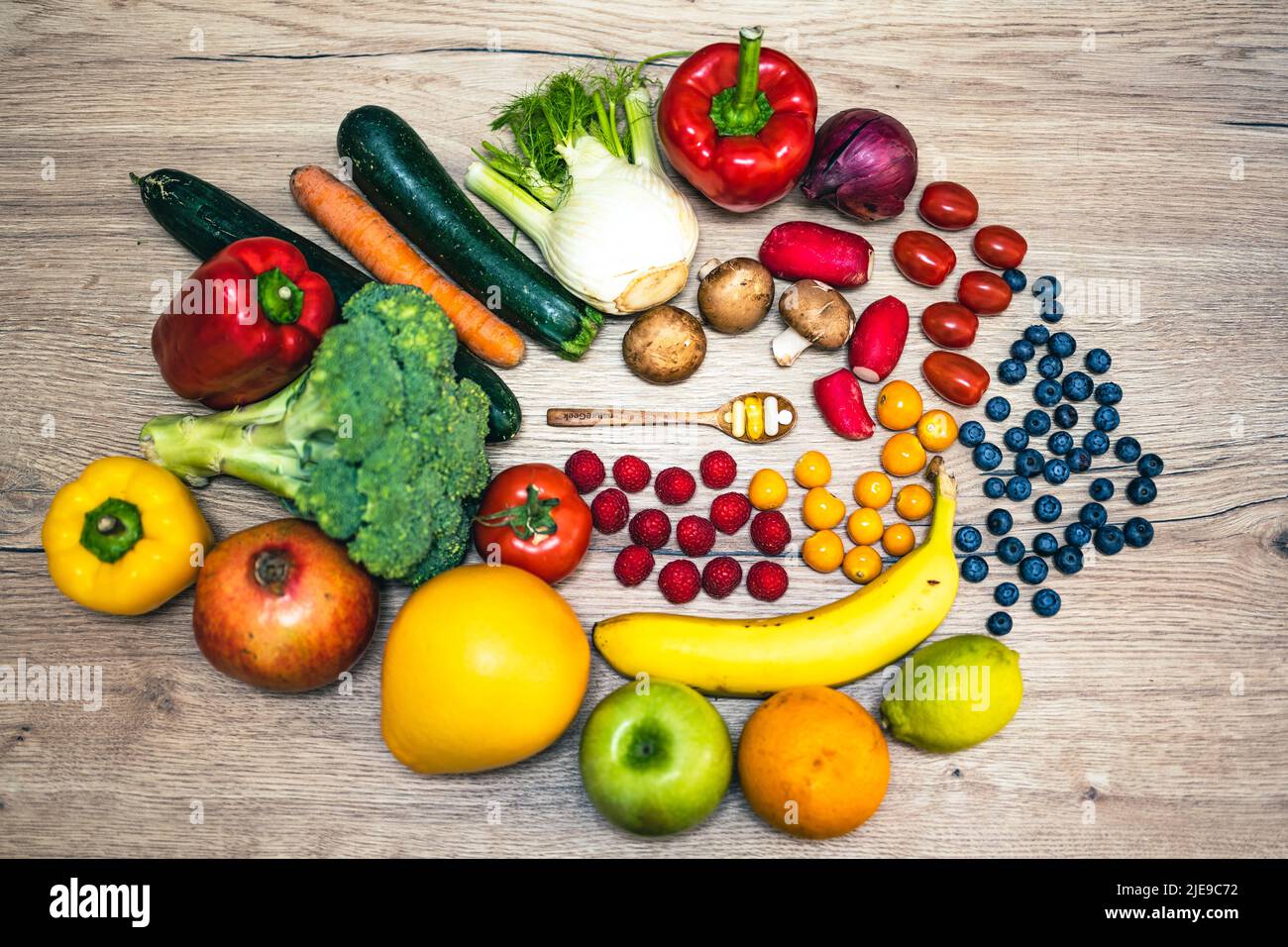 Une cuillère en bois avec des compléments alimentaires est placée dans le milieu des fruits et légumes frais, qui sont placés sur une table en bois. Compléments alimentaires enab Banque D'Images