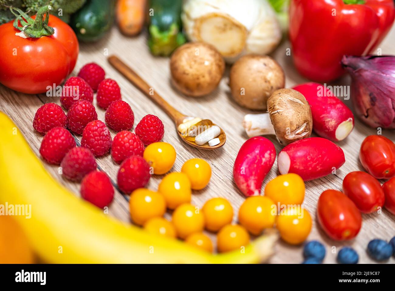 Une cuillère en bois avec des compléments alimentaires est placée dans le milieu des fruits et légumes frais, qui sont placés sur une table en bois. Compléments alimentaires enab Banque D'Images