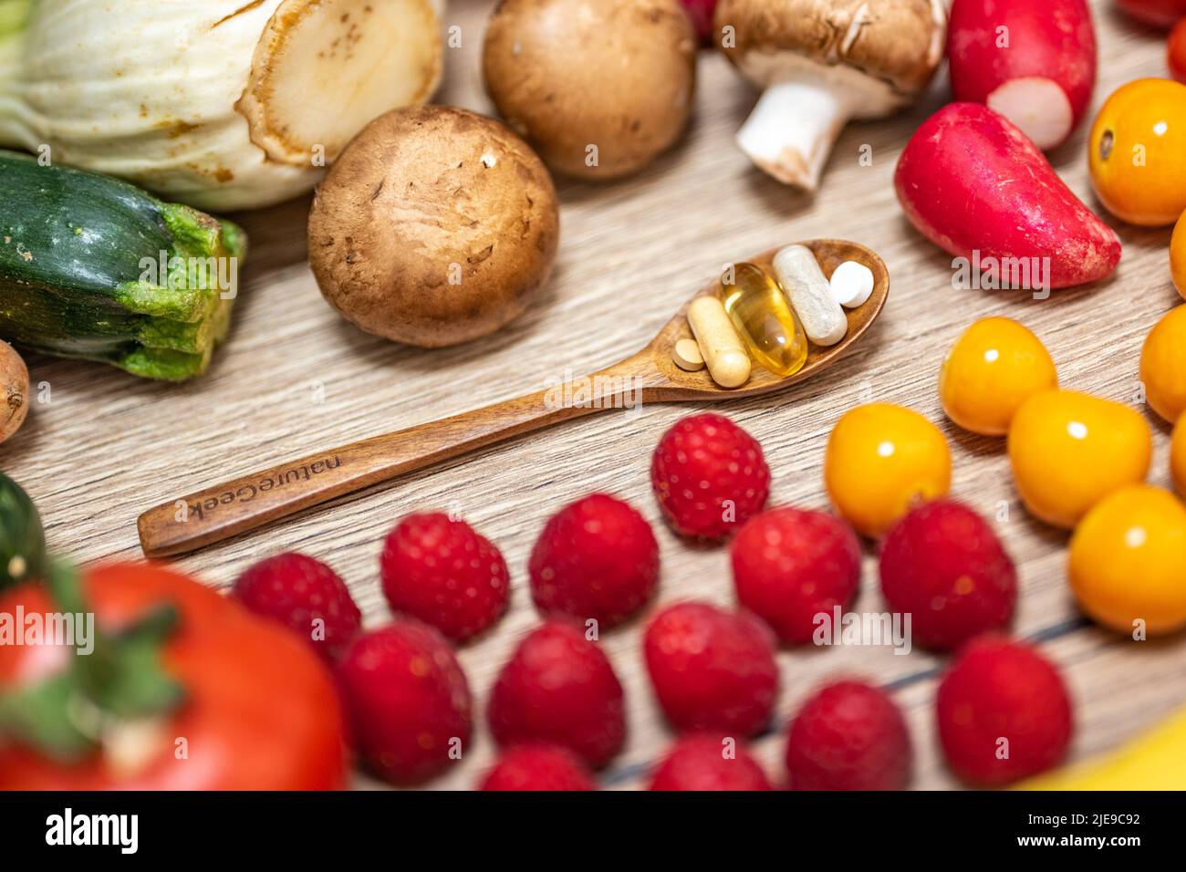 Une cuillère en bois avec des compléments alimentaires est placée dans le milieu des fruits et légumes frais, qui sont placés sur une table en bois. Compléments alimentaires enab Banque D'Images