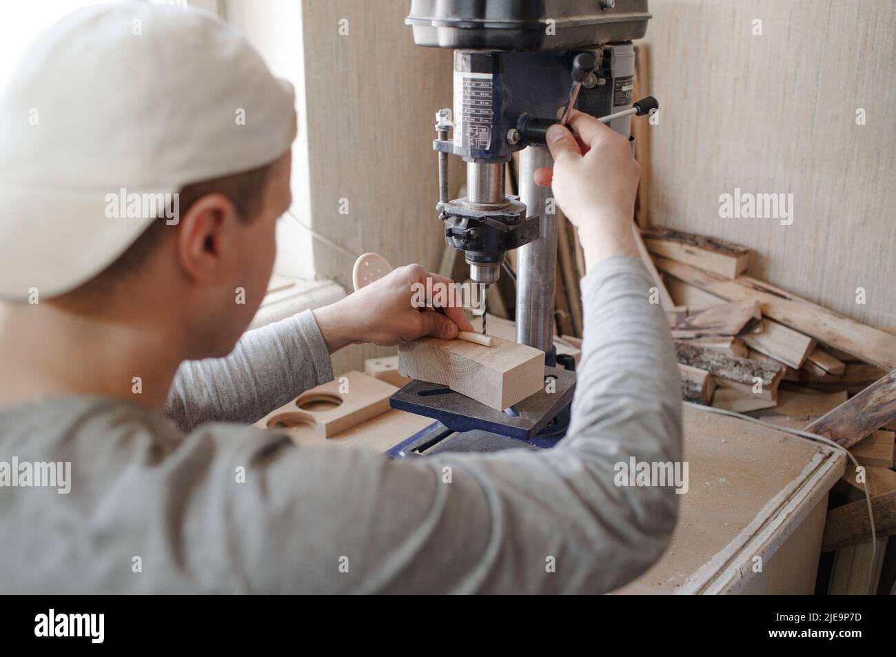 Un jeune charpentier utilise une machine de forage pour percer des trous dans une planche de bois Banque D'Images