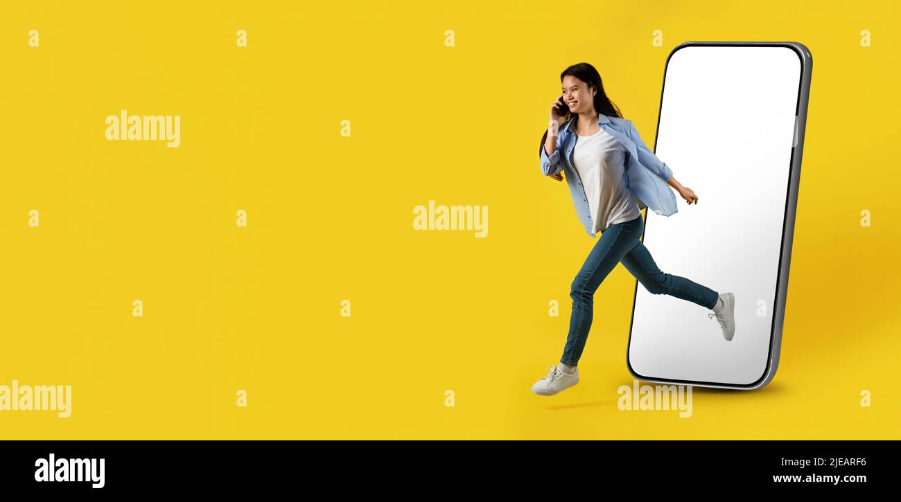 Jeune japonaise souriante et occupée, courant depuis un grand smartphone avec écran vide et parler au téléphone Banque D'Images