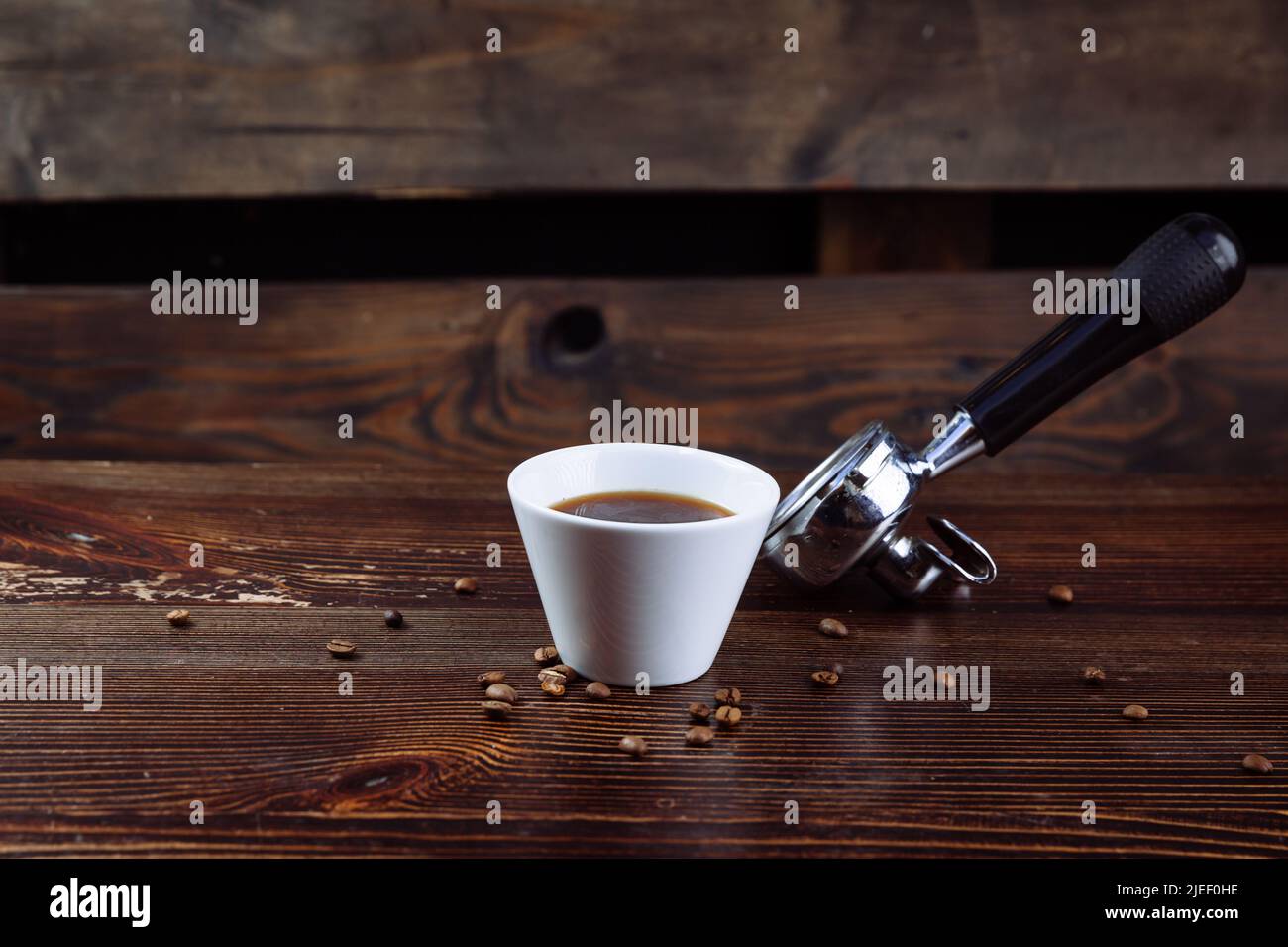 Une tasse de café noir, de grains de café torréfiés et un porte-machine à espresso sur fond sombre. Banque D'Images