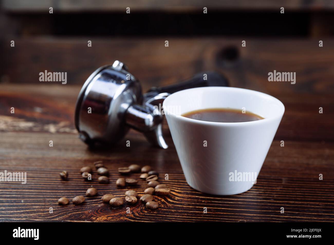 Une tasse de café noir, de grains de café torréfiés et un porte-machine à espresso sur fond sombre. Banque D'Images