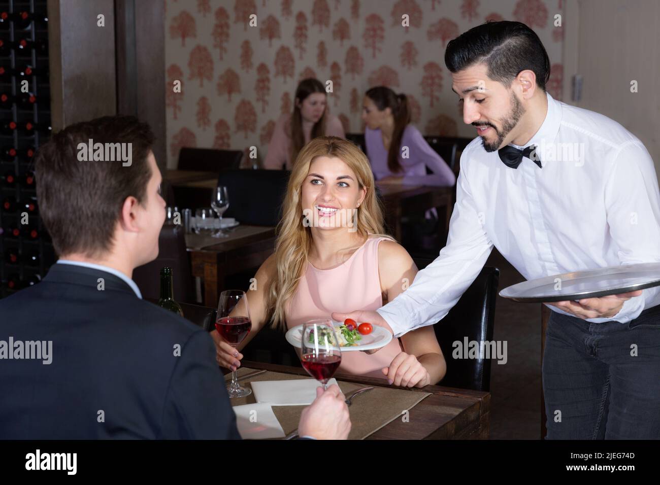 Poli garçon portant des plats commandés à smiling couple at restaurant Banque D'Images