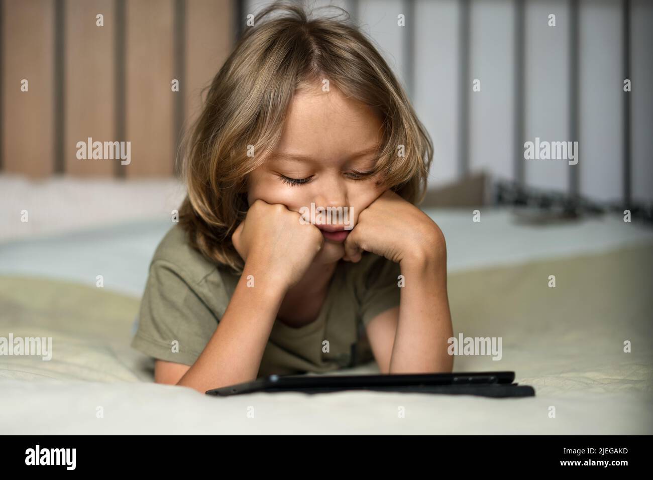Garçon allongé sur le lit à l'aide d'une tablette numérique pour jouer à des jeux ou regarder des dessins animés à la maison. Concept de sécurité Internet enfant. Enfant utilisant un équipement électronique. Contrôle parental. Formation en ligne. Banque D'Images