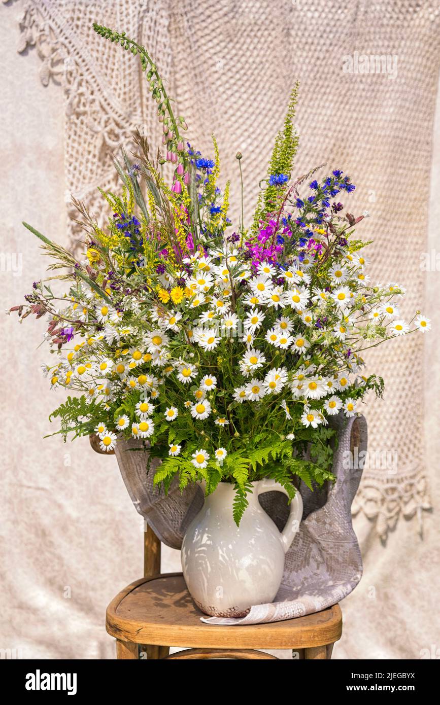 Bouquet de fleurs sauvages avec des chamomiles, des cornflowers, du renfgant, du thé ivan, des herbes dans une carafe blanche sur une chaise. Arrangement fait par un fleuriste. Banque D'Images