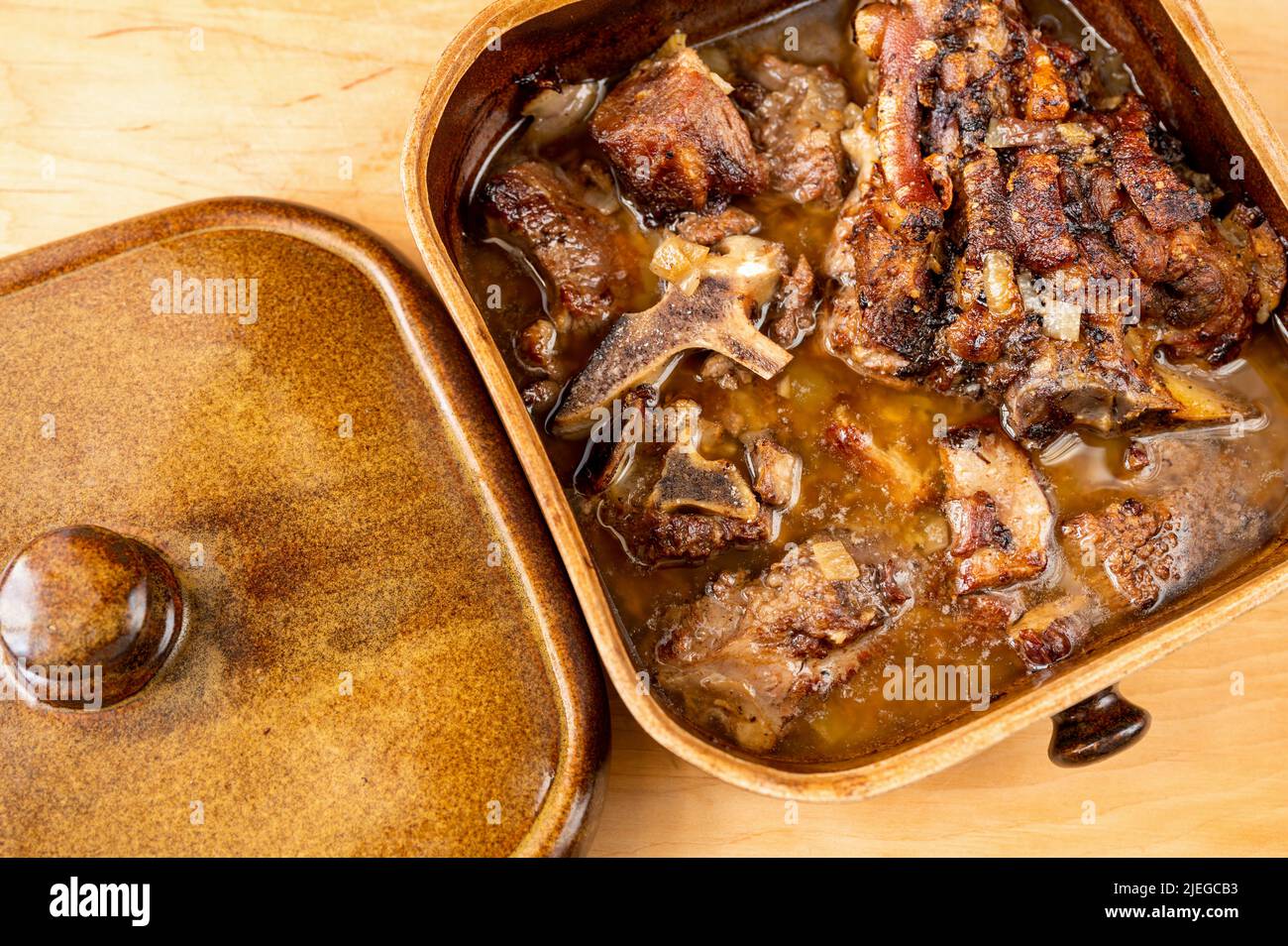 Ouvrez une poêle rustique en faïence pleine de viande de porc juteuse graisseuse sur une table en bois, en gros plan. Banque D'Images