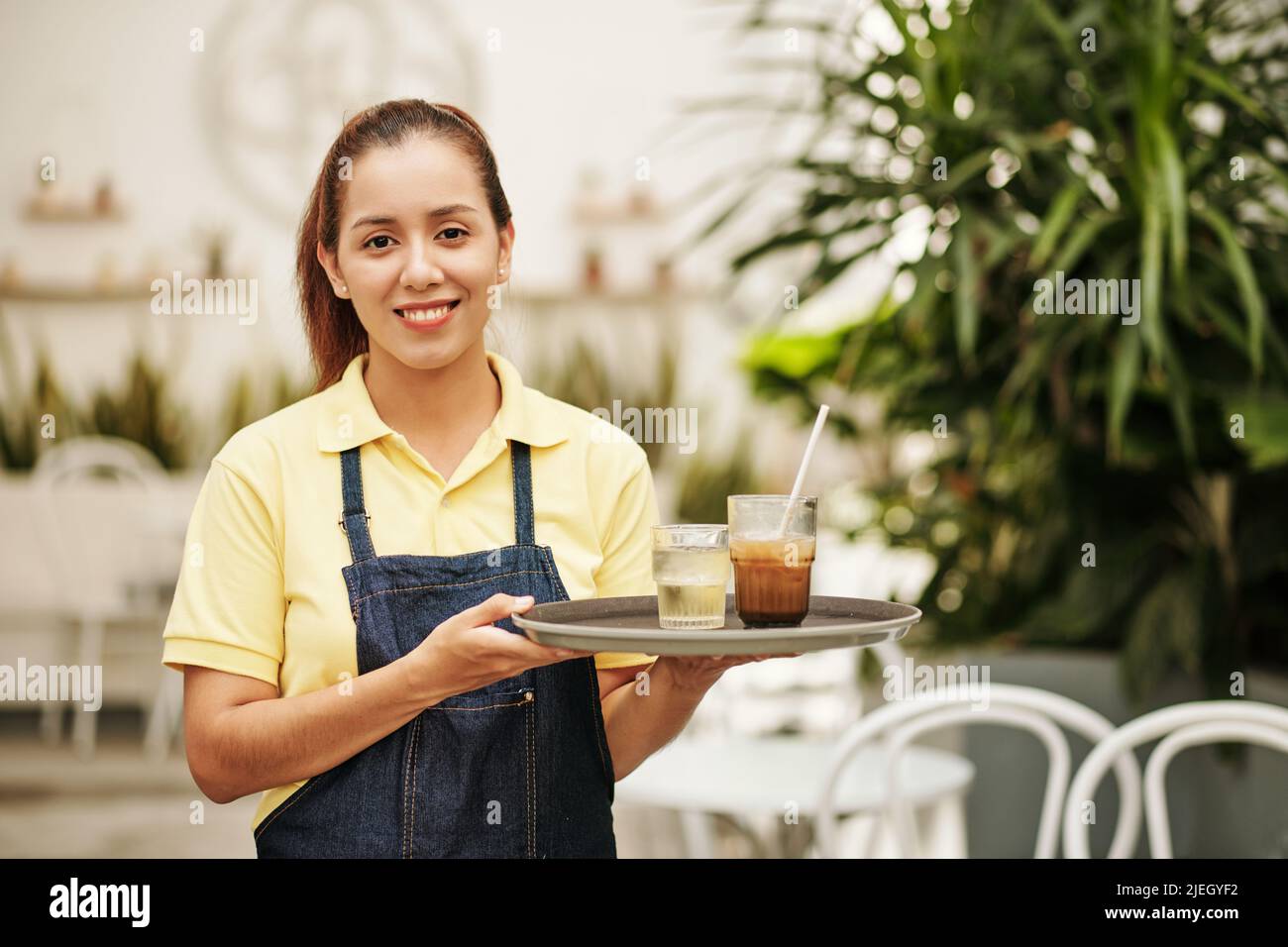Portrait d'une serveuse souriante tenant un plateau avec de l'eau froide et du café glacé pour le client Banque D'Images