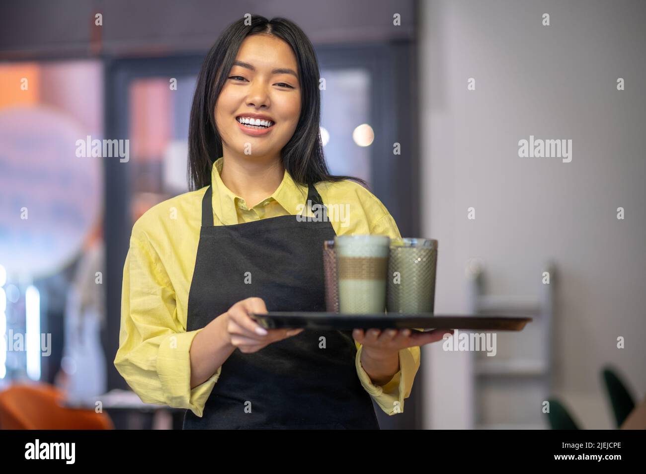 Femme avec plateau souriant à l'appareil photo debout dans le café Banque D'Images