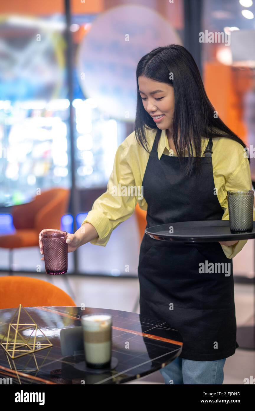 Femme souriante abaissant un verre de cappuccino sur la table Banque D'Images