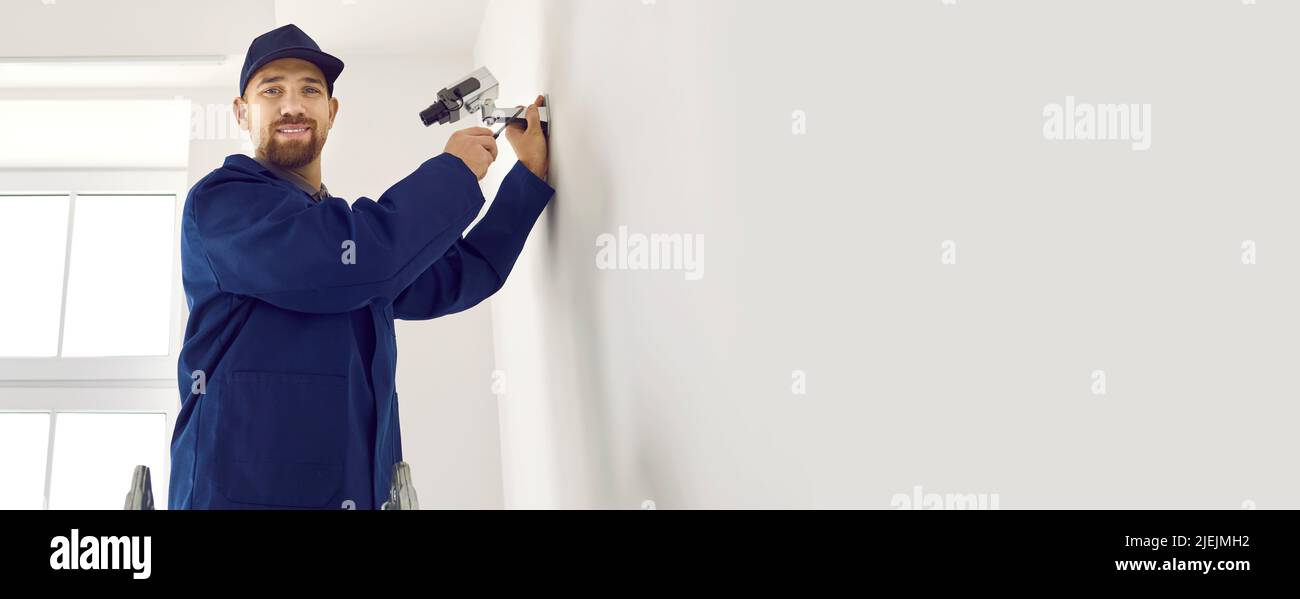 Un jeune technicien professionnel installe une caméra de surveillance à l'intérieur d'un bureau ou d'un appartement. Banque D'Images