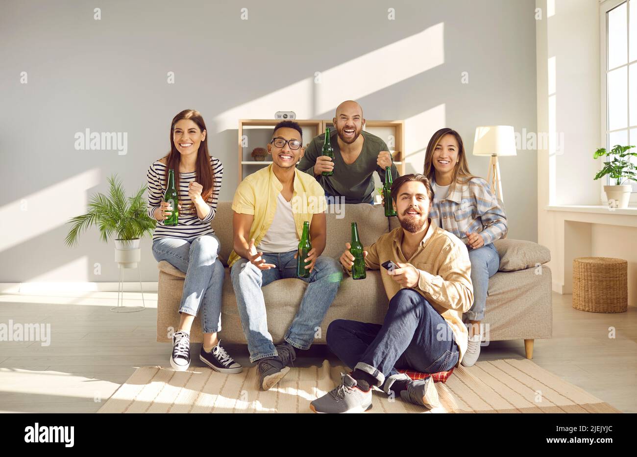Des amis multiraciaux, hommes et femmes, regardent des compétitions sportives à la télévision à la maison. Banque D'Images