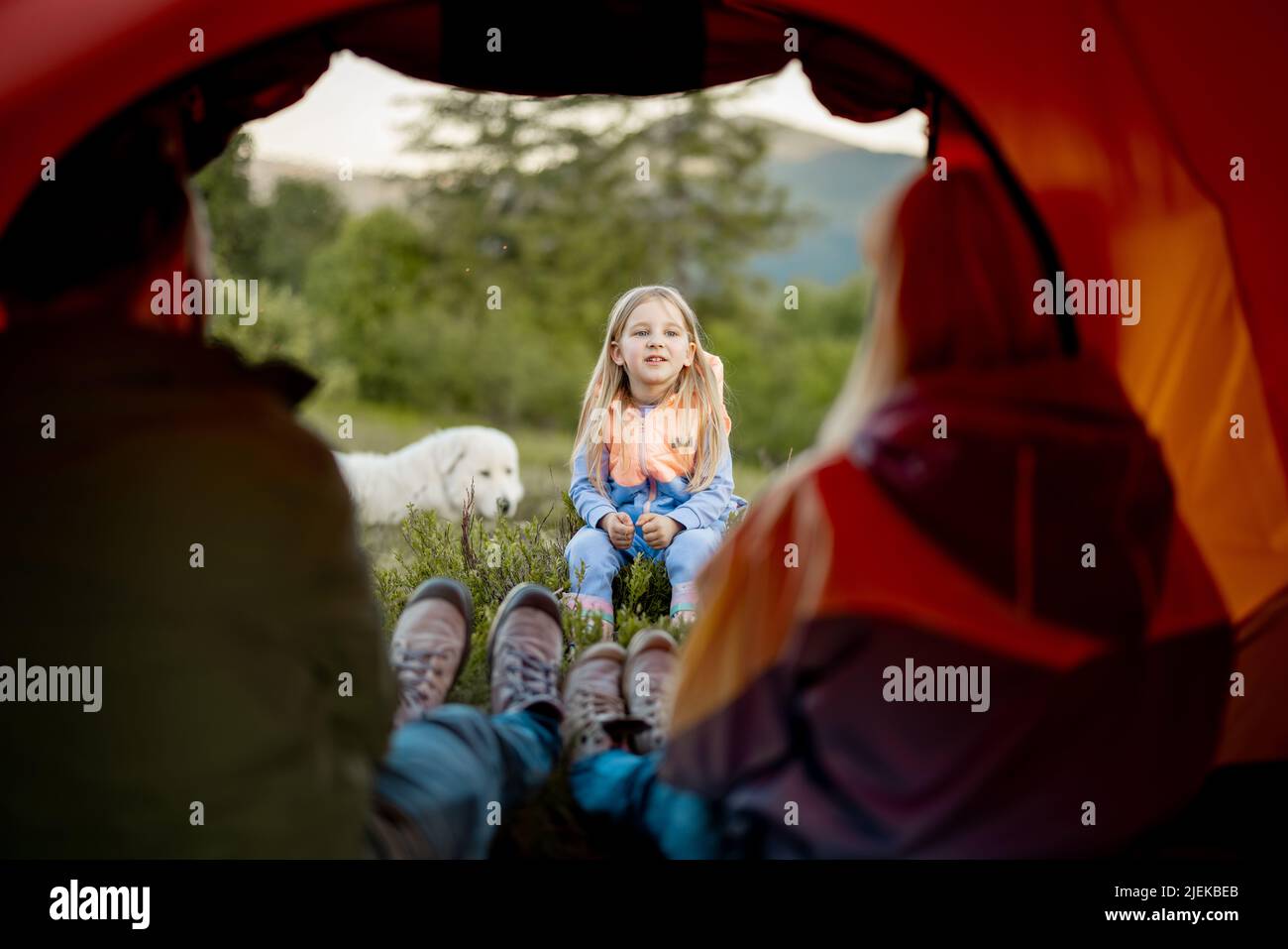 Une petite fille mignonne raconte une histoire à ses parents qui s'assoient dans une tente de camping Banque D'Images