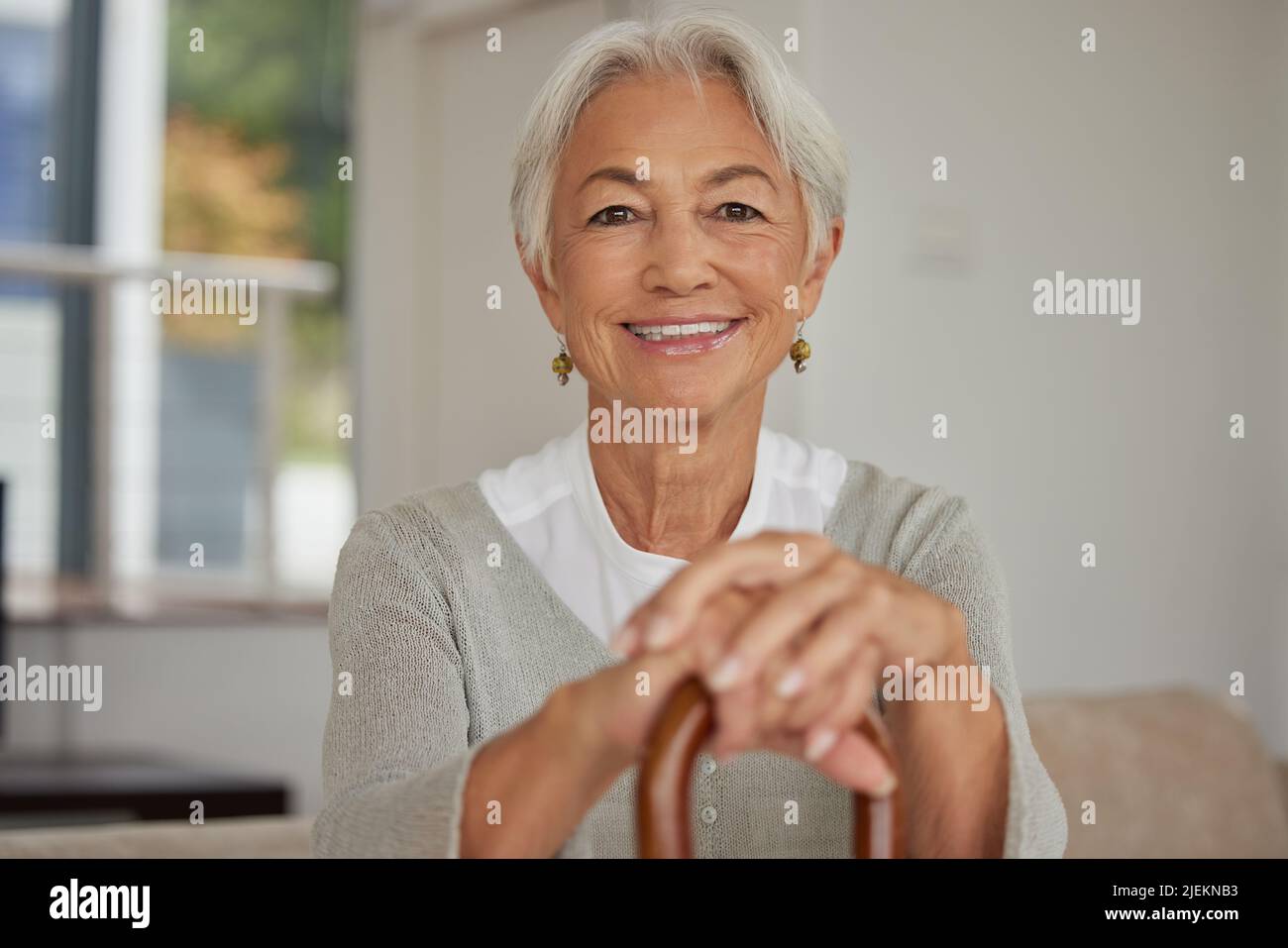 Femme sénior à la retraite se détendant à la maison. Bonne vieille femme souriante tenant une canne à pied et regardant la caméra avec positivité. Insouciant et mûr Banque D'Images