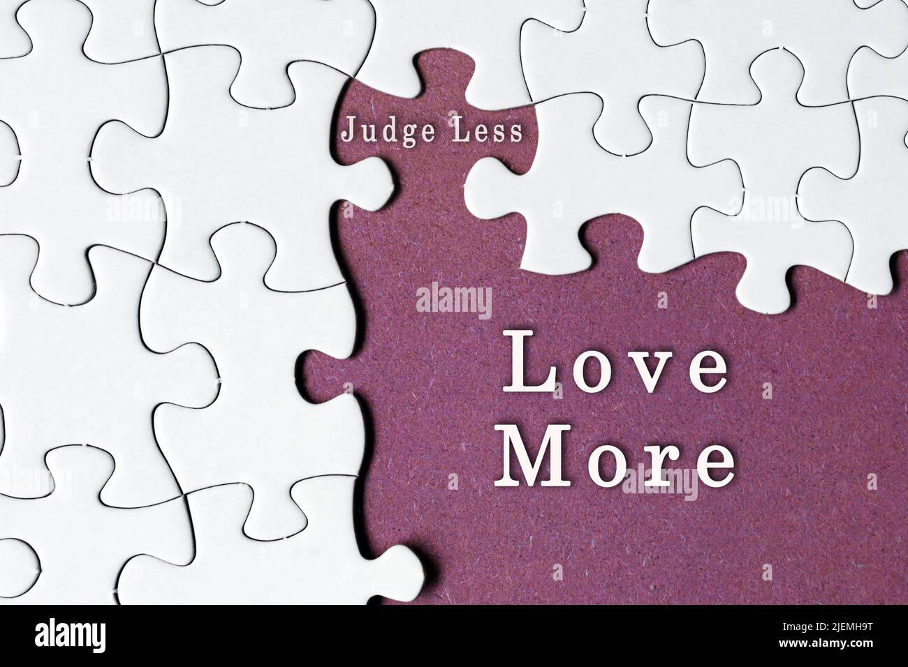 Citation motivationnelle sur puzzle blanc avec quelques pièces manquantes sur fond violet - juge moins amour plus. Banque D'Images