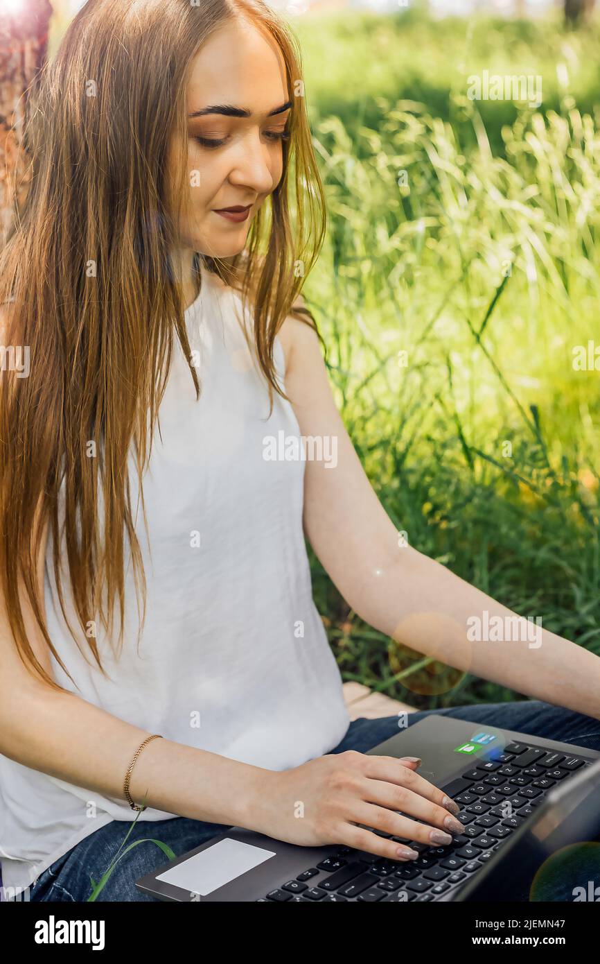 Sur la bannière, une jeune fille travaille avec un ordinateur portable dans l'air frais du parc, assis sur la pelouse. Le concept de travail à distance. Travailler en tant que freelance. T Banque D'Images